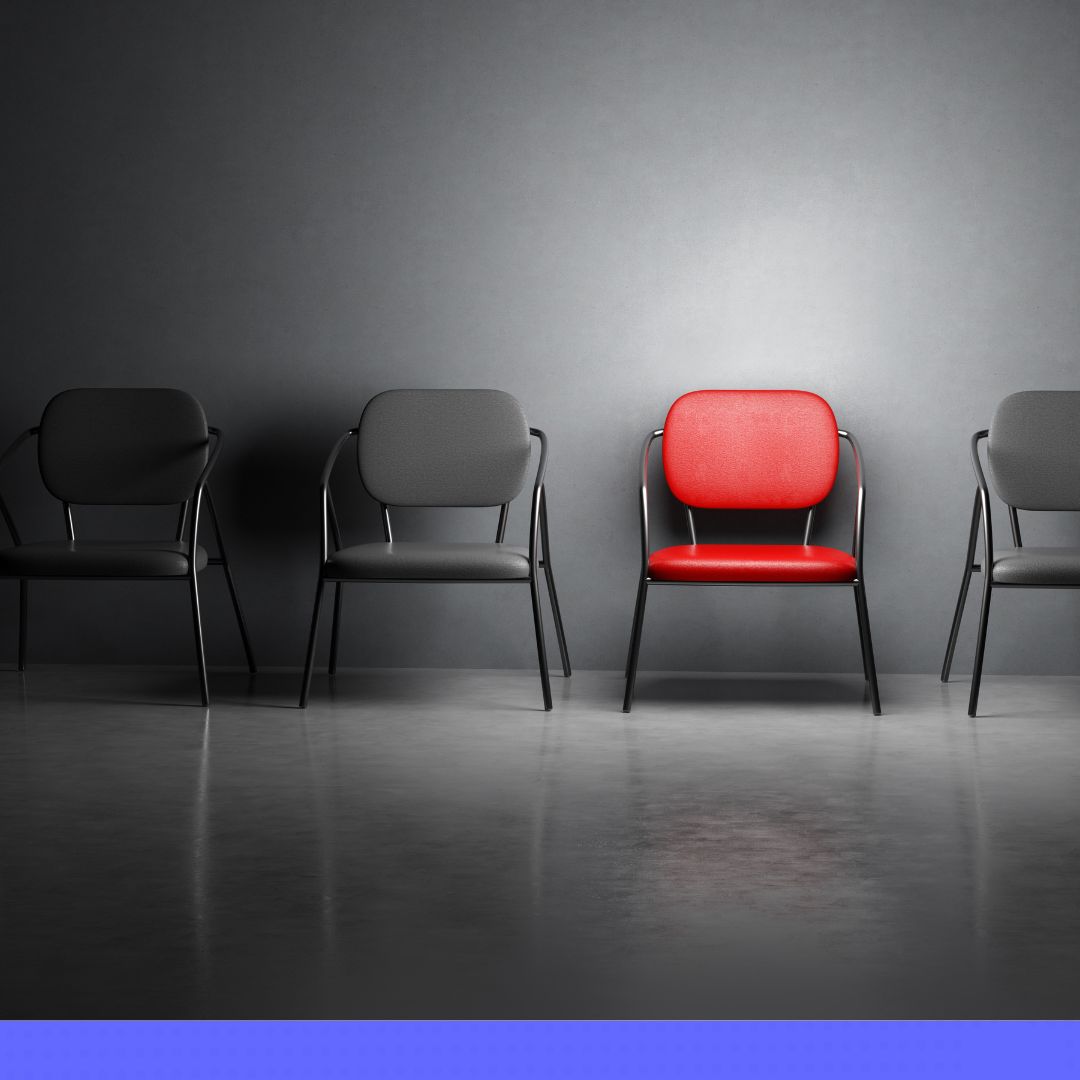 4 chairs against a dark wall with one chair colored bright red remaining chairs in gray and dark lighting